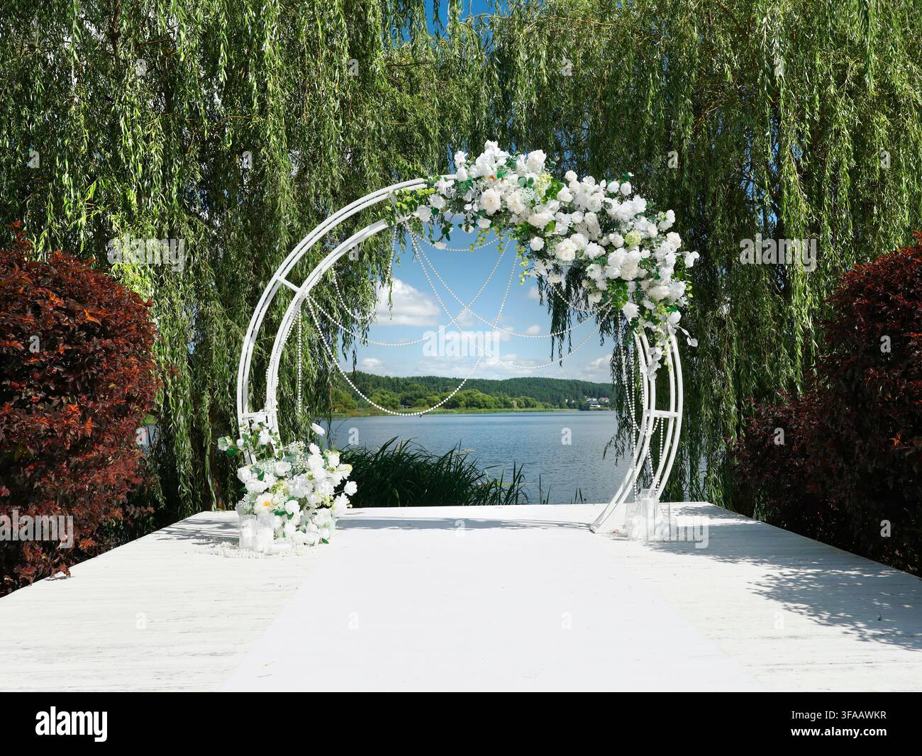 Lieu de mariage de luxe avec une arche fleurie romantique sur une jetée en bois blanc à côté d’un lac pittoresque. Lieu élégant pour une cérémonie de mariage avec un blanc exquis Banque D'Images