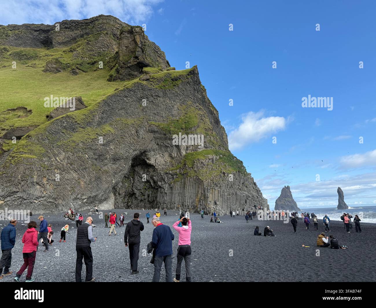 REYNISFJARA, ISLANDE - 10 AOÛT 2025 : Les touristes se rassemblent sur la plage de sable noir de Reynisfjara, connue pour ses colonnes de basalte dramatiques et la vue sur - Image de stock capturée avec un smartphone