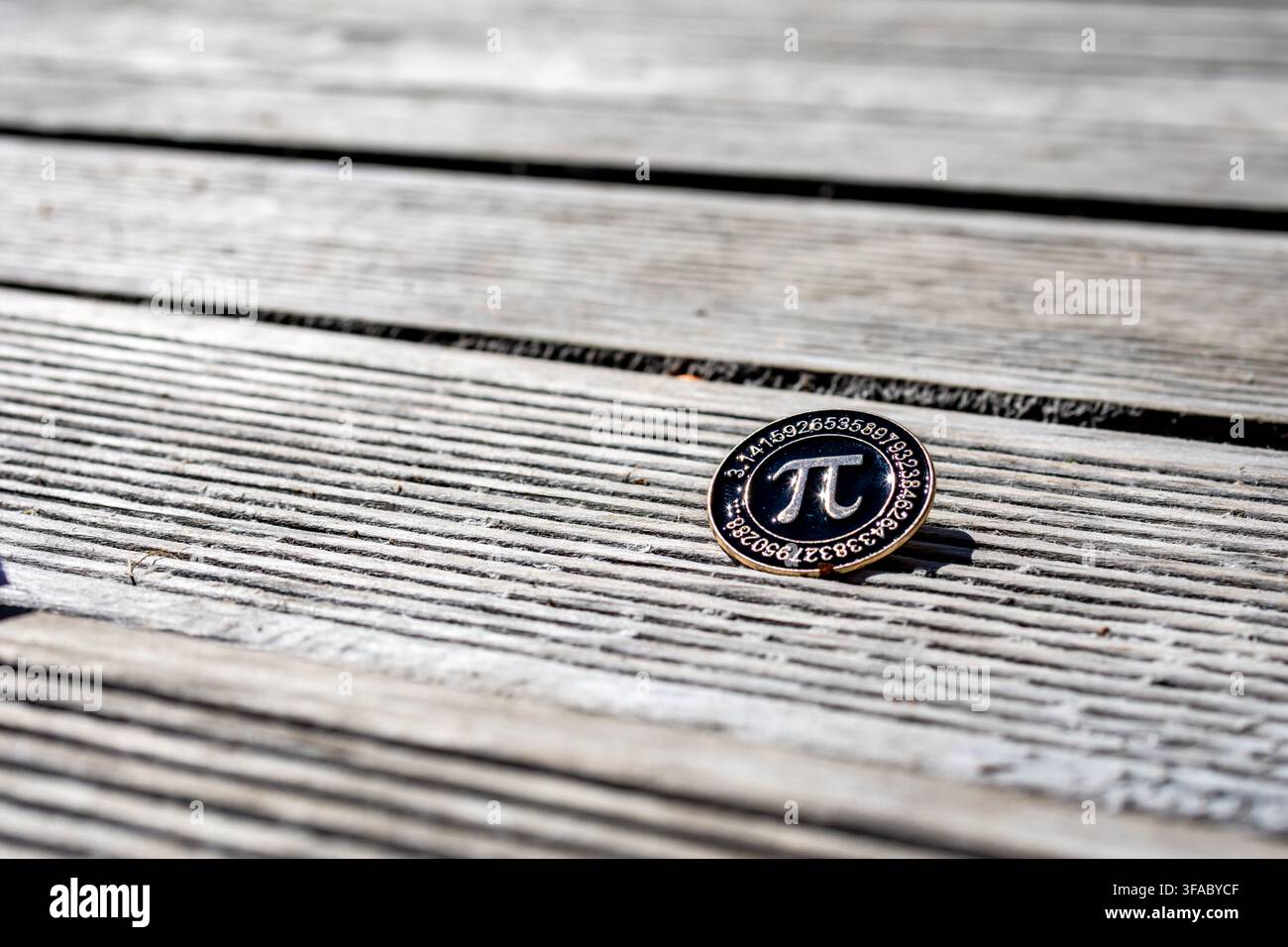 Une petite épingle en métal avec le symbole pi repose sur des planches de bois érodées sous une lumière solaire vive suggérant la fierté mathématique et l'identité académique minimaliste Banque D'Images