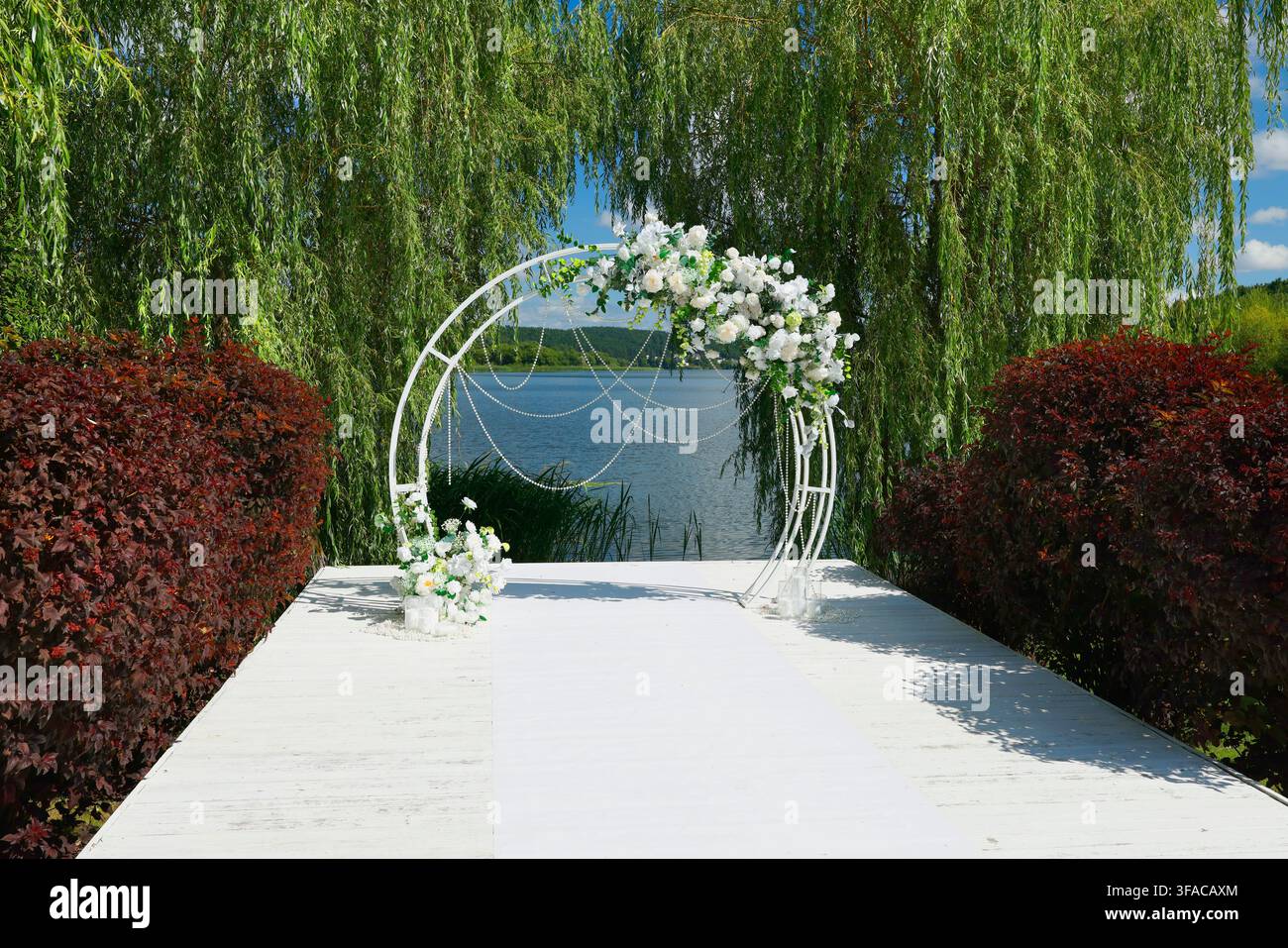 Lieu de mariage de luxe avec une arche fleurie romantique sur une jetée en bois blanc à côté d’un lac pittoresque. Lieu élégant pour une cérémonie de mariage avec un blanc exquis Banque D'Images