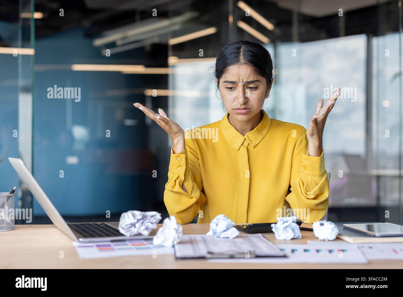 Jeune femme indienne contrariée et inquiète assise au bureau dans le bureau et regardant un papier froissé. Banque D'Images