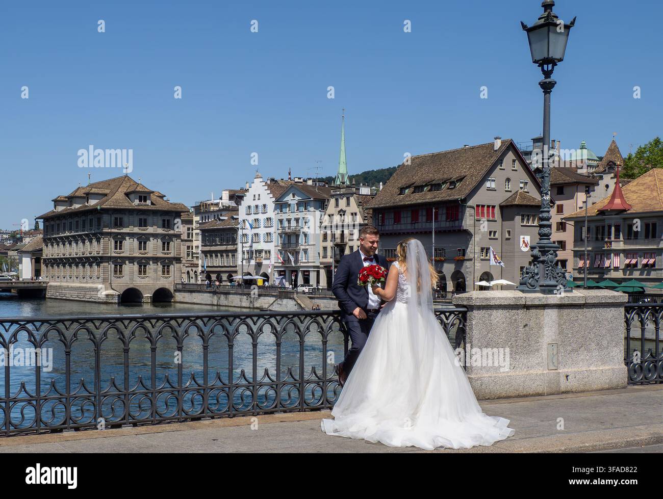 Mariée en robe de mariée blanche posant avec son mari à côté d'une rambarde de pont en fer forgé ornée surplombant la rivière Limmat à Zurich. Banque D'Images