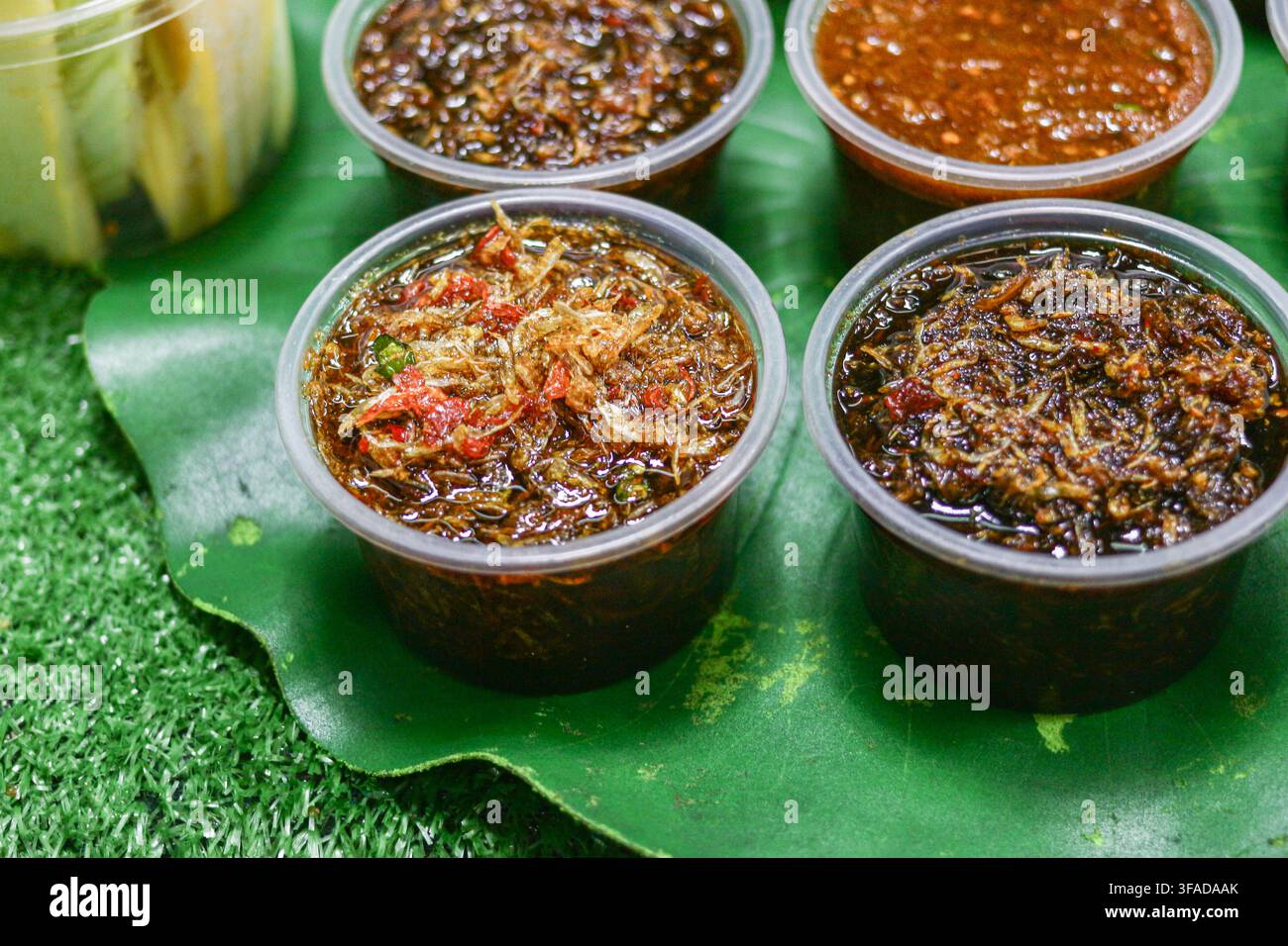 Des rangées de sauces thaïlandaises épicées se trouvent dans des gobelets en plastique transparent sur un plateau à motifs de feuilles de bananier, une photo de condiment en gros plan. Banque D'Images