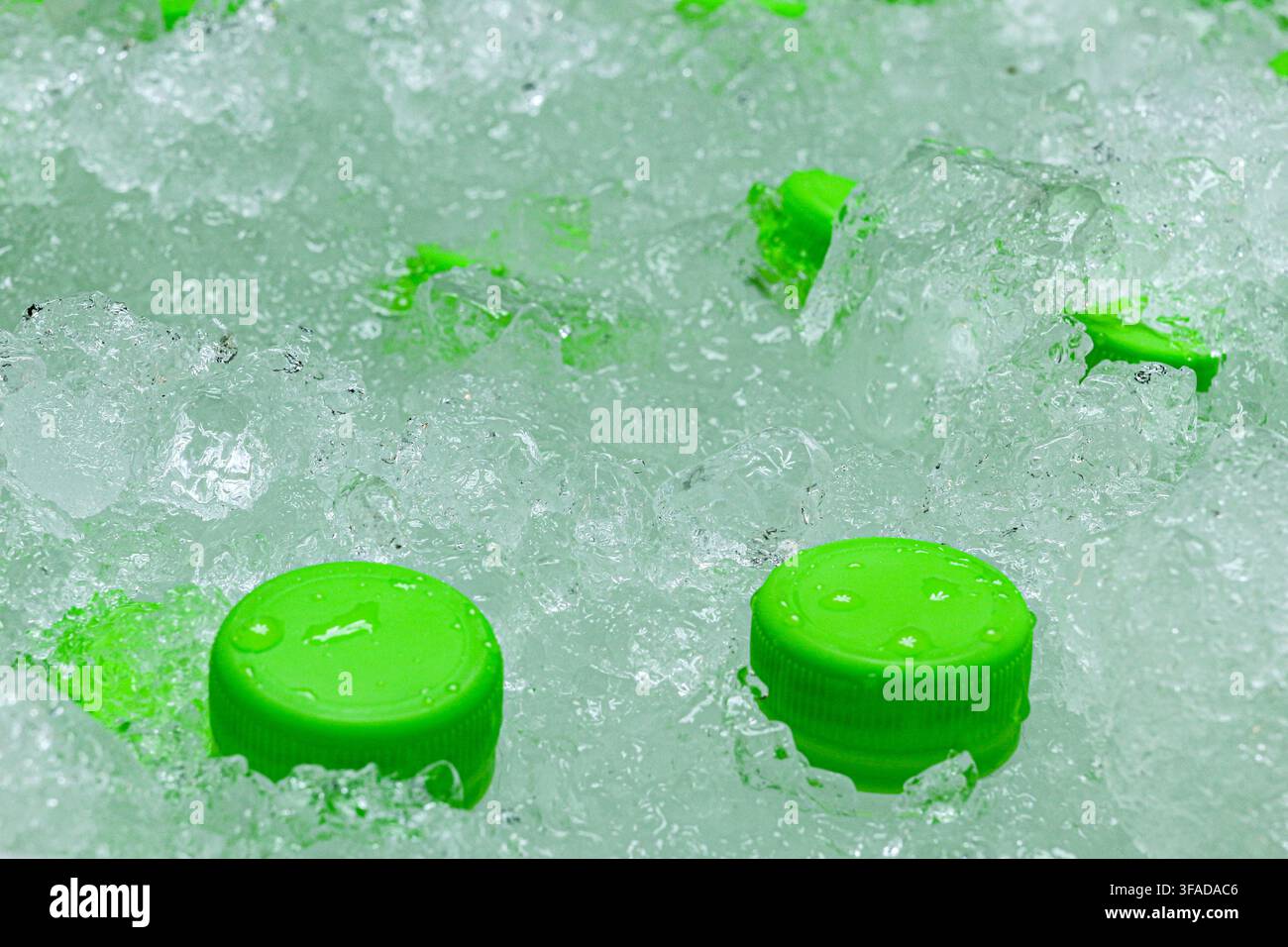 Gros plan de bouchons de bouteilles verts dans de la glace pilée claire avec des gouttelettes d'eau. Texture abstraite pour des thèmes de boissons fraîches et de rafraîchissements d'été. Banque D'Images