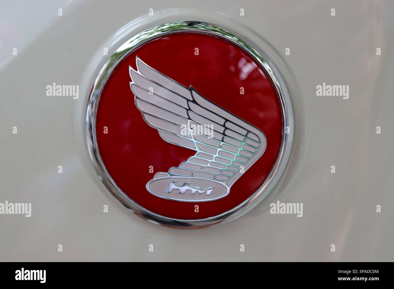 Close up de la marque Honda motorcycles, montrant une aile blanche élégante avec les lettres « HM » à l'intérieur d'un ovale blanc, le tout sur un fond rouge. Banque D'Images