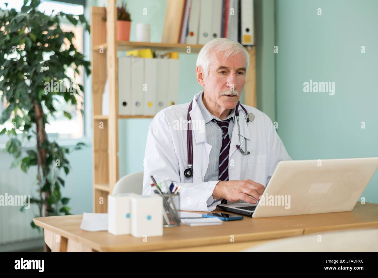 Médecin senior travaille sur un ordinateur portable dans le bureau de la clinique, à la recherche d'informations sur les maladies sur Internet Banque D'Images