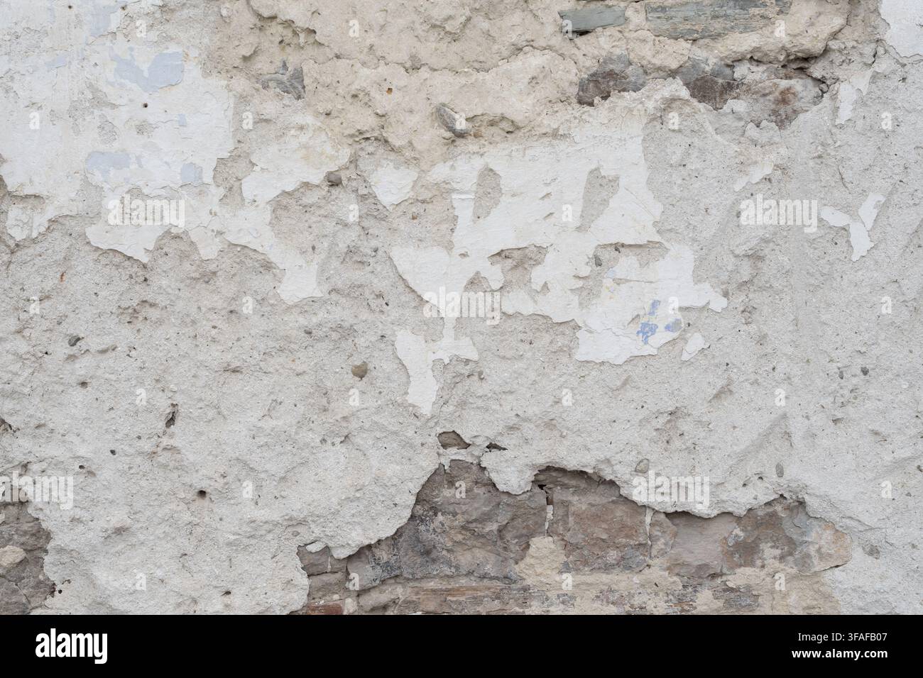 Détail d'un vieux mur endommagé avec du plâtre s'effritant, de la peinture s'écaillant et de la maçonnerie en brique et pierre exposée Banque D'Images