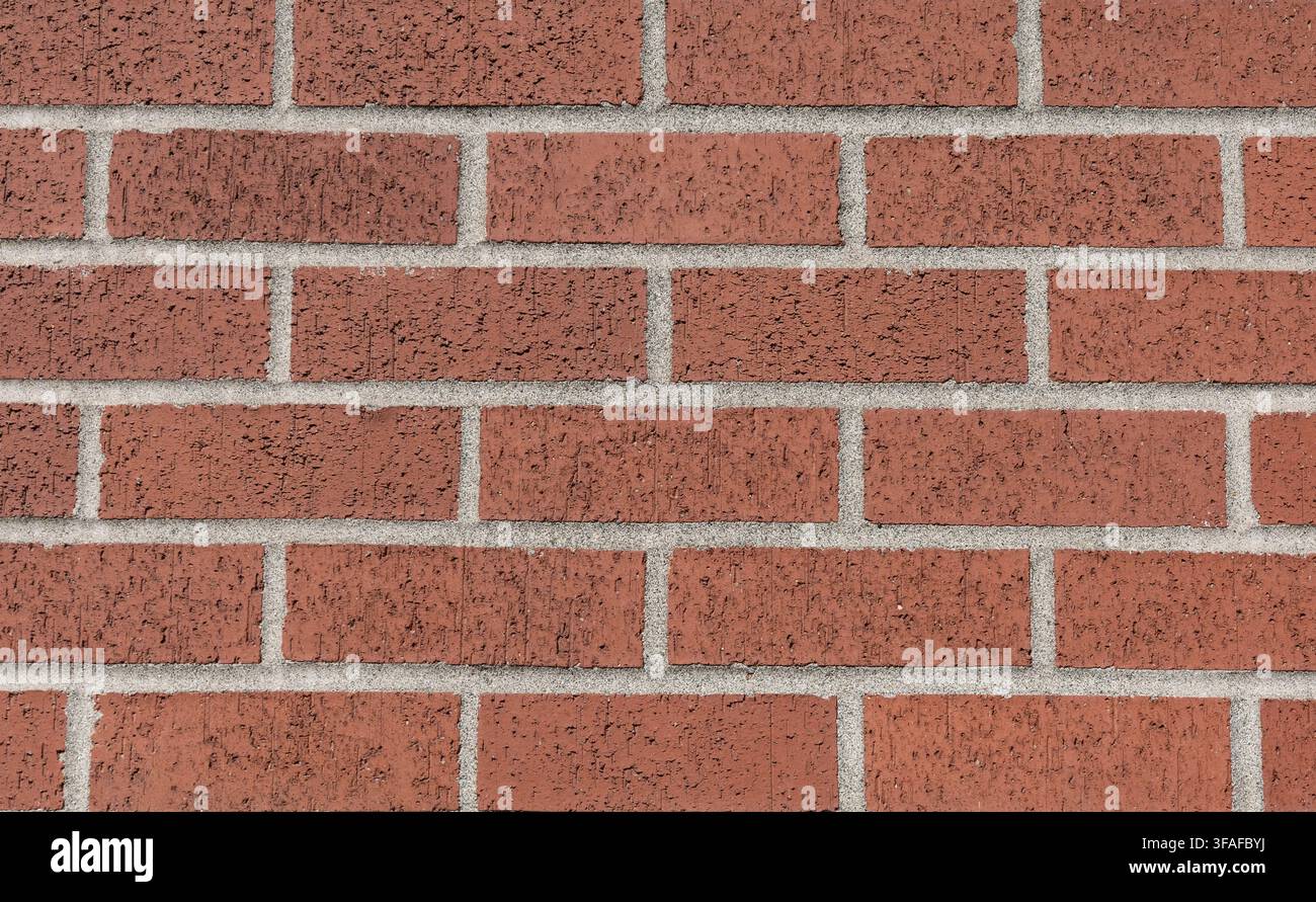 Vue rapprochée en face d'un mur de briques rouges avec des joints de mortier gris formant un motif de maçonnerie répétitif. Banque D'Images