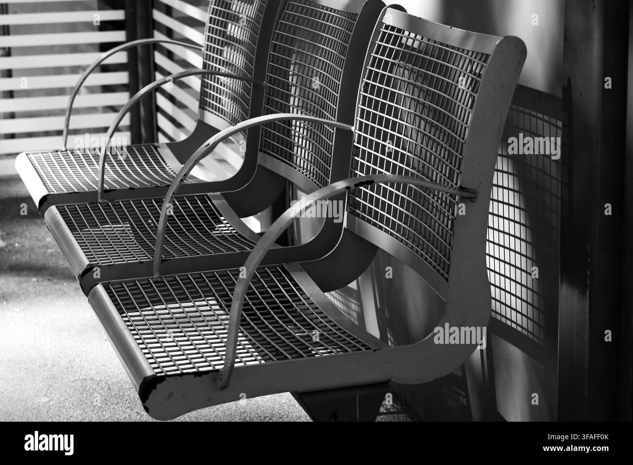 Bancs en grille métallique vides à une station de transport public en noir et blanc Banque D'Images