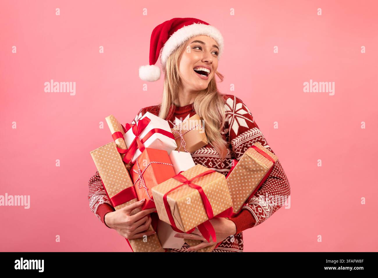 Belle femme caucasienne en tenue de Noël tenant pile de cadeaux de Noël emballés sur fond rose. Soldes des fêtes Banque D'Images