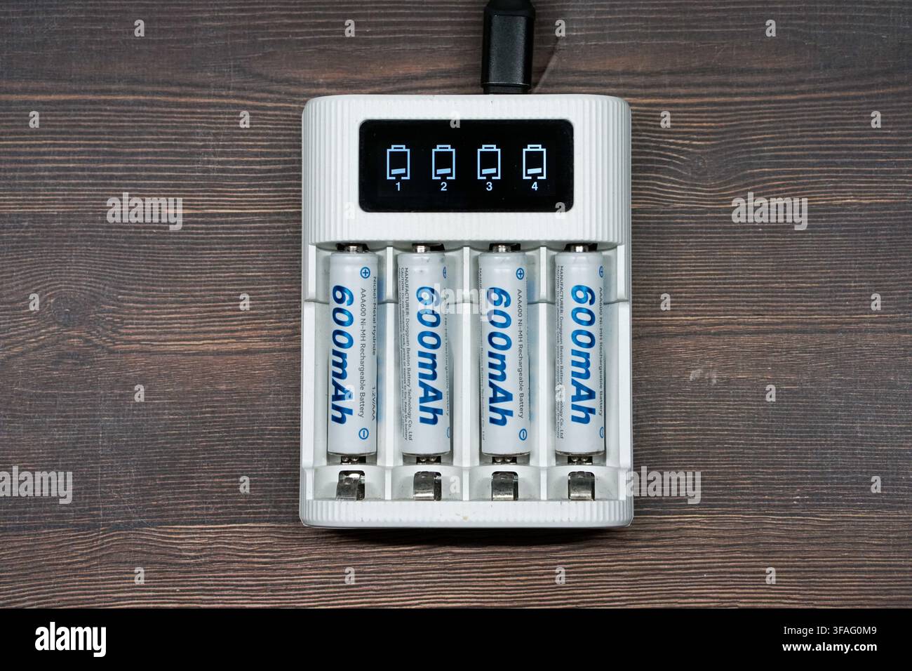 Vue aérienne de quatre piles rechargeables Ni-MH dans un chargeur intelligent blanc moderne avec affichage numérique du statut, posées sur une surface en bois sombre pour eff Banque D'Images