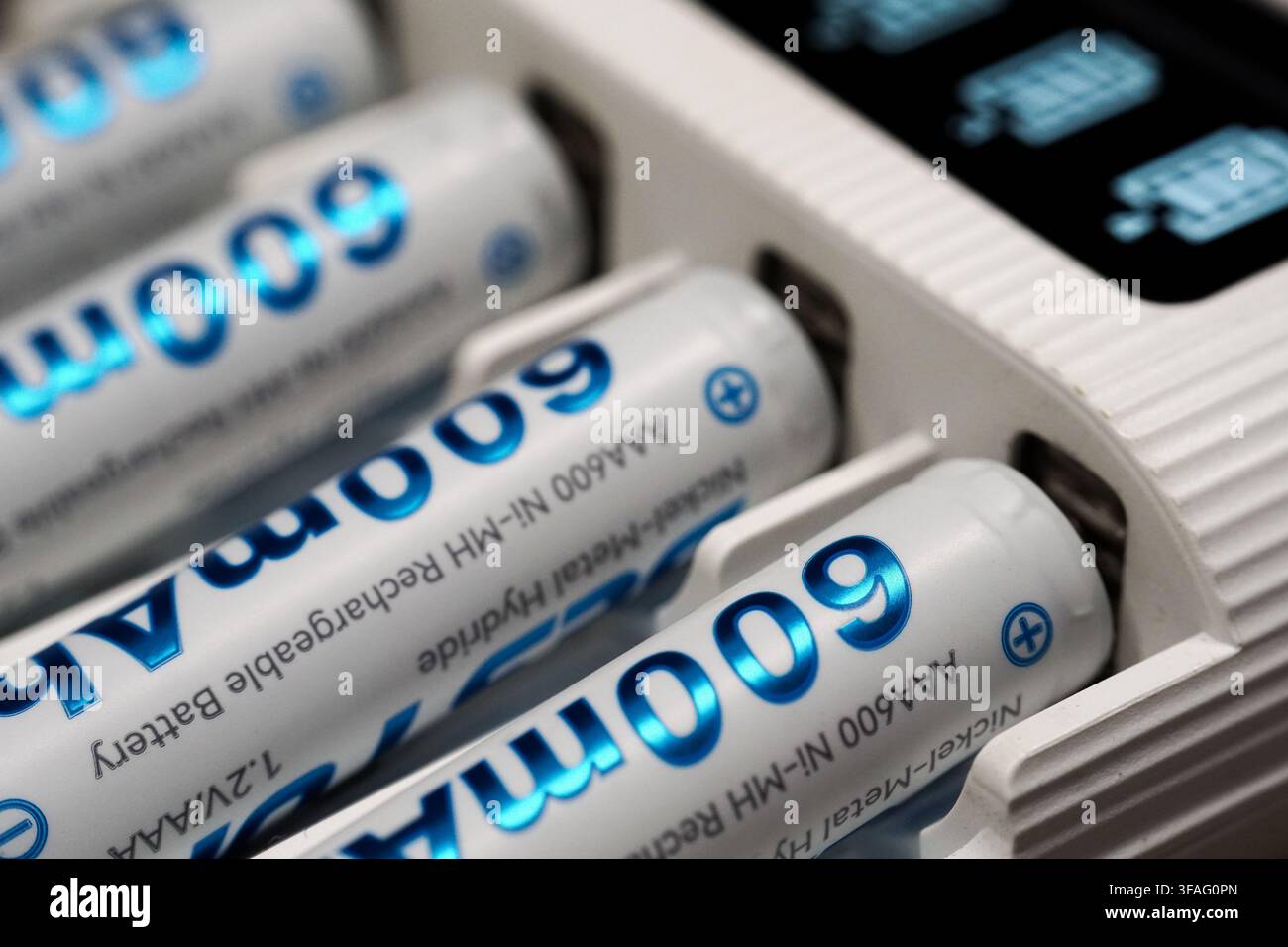 Prise de vue macro de piles AAA Ni-MH argentées avec texte bleu en train de charger dans un chargeur intelligent blanc avec écran numérique. Banque D'Images