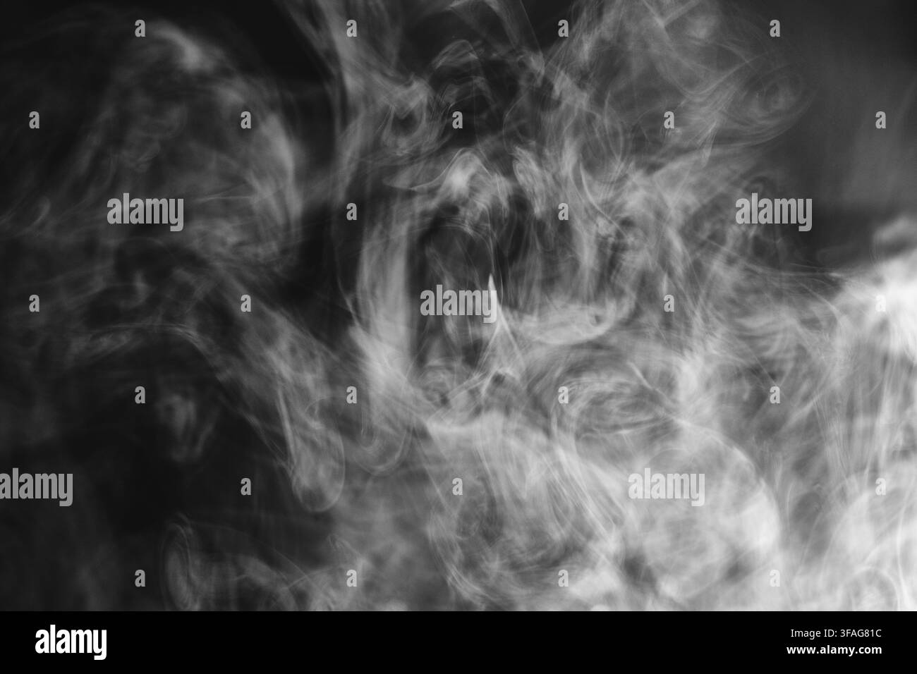 Des tourbillons de fumée blanche abstraits et des volutes de vapeur dérivant sur un fond sombre créant une texture dramatique et atmosphérique avec des motifs fluides et doux. Banque D'Images