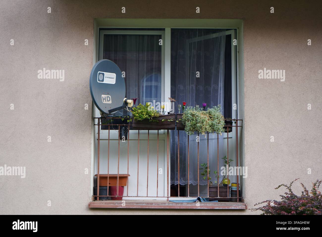 Fenêtre d'appartement résidentiel avec antenne parabolique, porte vitrée avec rideaux et plantes ornementales en pot sur le balcon étroit. Banque D'Images