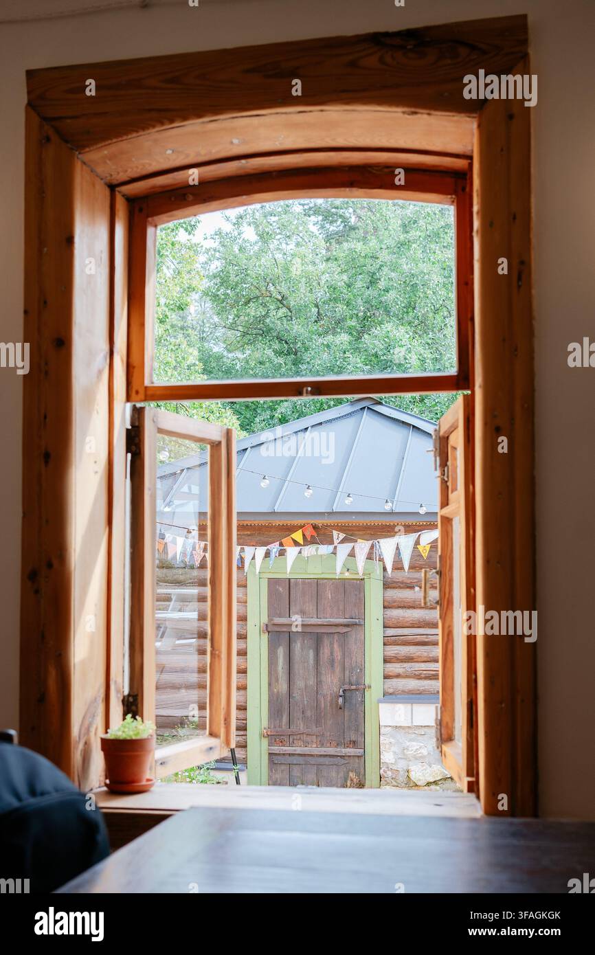 vue extérieure sereine depuis l'intérieur d'une cabane rustique, avec fenêtre en bois ouverte, arbres verts à l'extérieur, structure de toit en métal et plante en pot à l'intérieur Banque D'Images