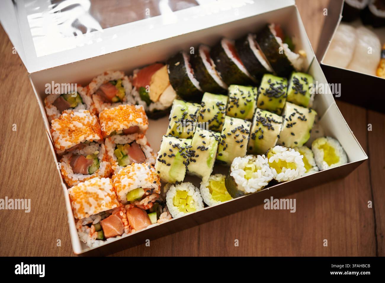 Assortiment de sushi japonais servi dans une boîte à emporter, comprenant des rouleaux maki, des rouleaux de concombre, des sushi garnis de roe de poisson tobiko orange et des nigiri aux crevettes. Banque D'Images