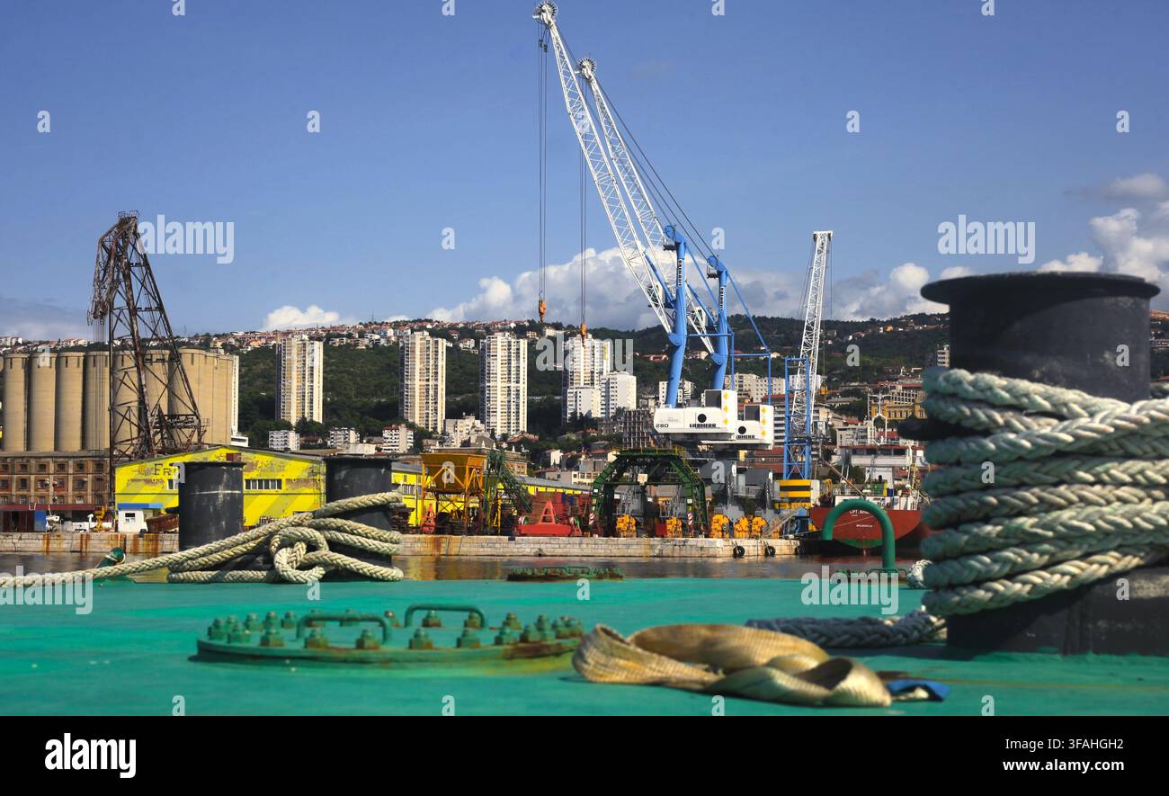 Boulon d'amarrage avec des cordages sur le pont, avec des grues portuaires et un arrière-plan de ciel urbain au port de Rijeka, baie de Kvarner, Croatie. Banque D'Images