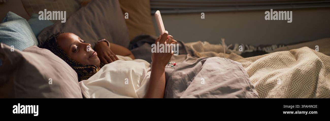 En-tête d'une femme noire allongée dans un lit utilisant un smartphone pour les réseaux sociaux Banque D'Images