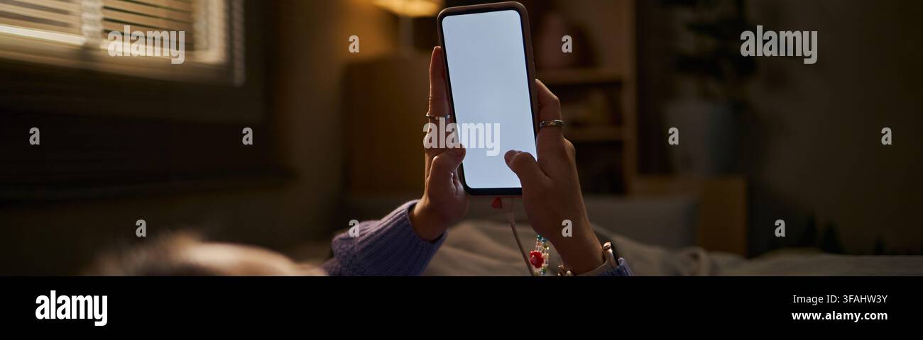 En-tête de femme tenant un smartphone avec écran vierge dans un lit la nuit Banque D'Images