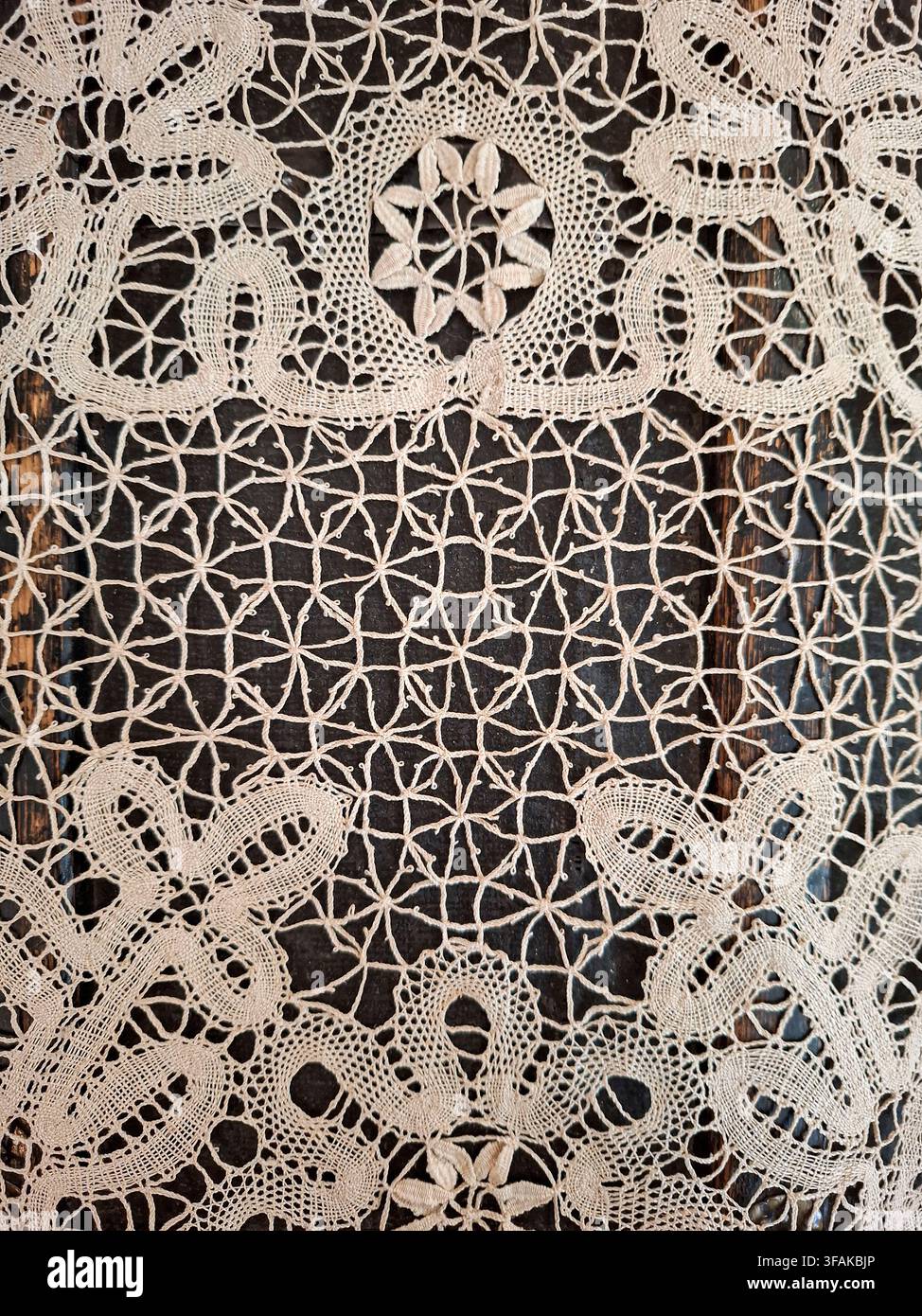 Une nappe en dentelle vintage arborant un motif de broderie florale est posée sur une table en bois sombre. Le design détaillé met en valeur le savoir-faire et un Banque D'Images
