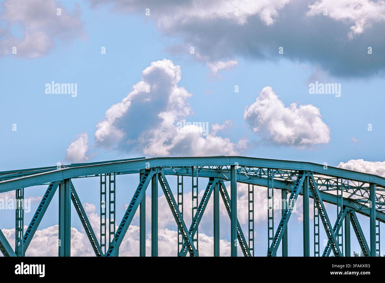 Pont à treillis en acier avec de grandes poutres et des poutres triangulaires. Ciel bleu clair avec des nuages blancs. Des lignes géométriques fortes créent une structure technique. Banque D'Images