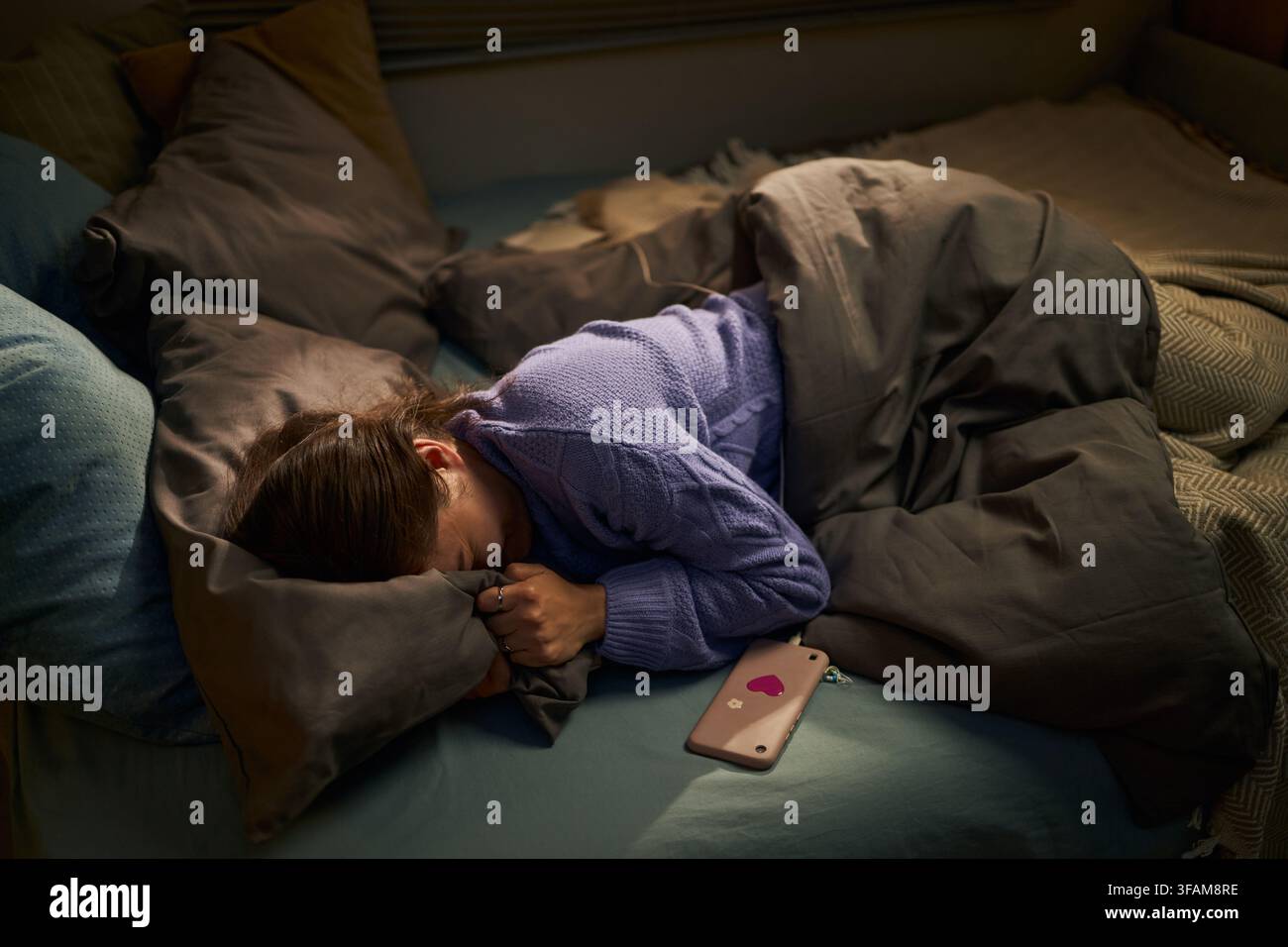 Femme déprimée allongée dans son lit avec un smartphone souffrant d'insomnie Banque D'Images