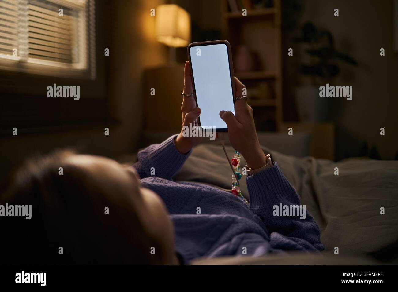 Femme allongée dans le lit utilisant un smartphone avec écran vide la nuit Banque D'Images