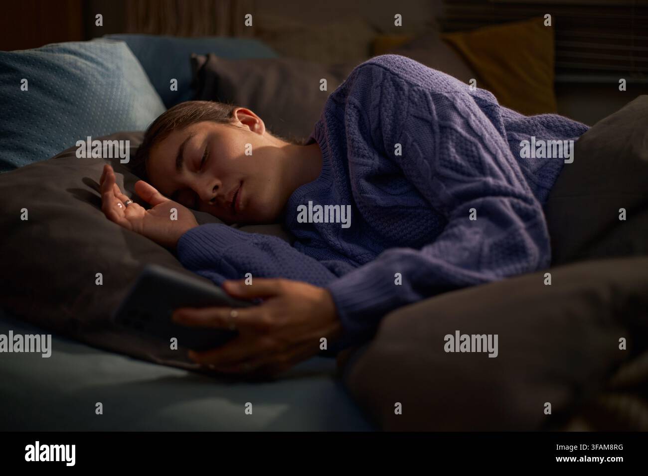 Femme dormant dans un lit tout en tenant un smartphone dans la main Banque D'Images
