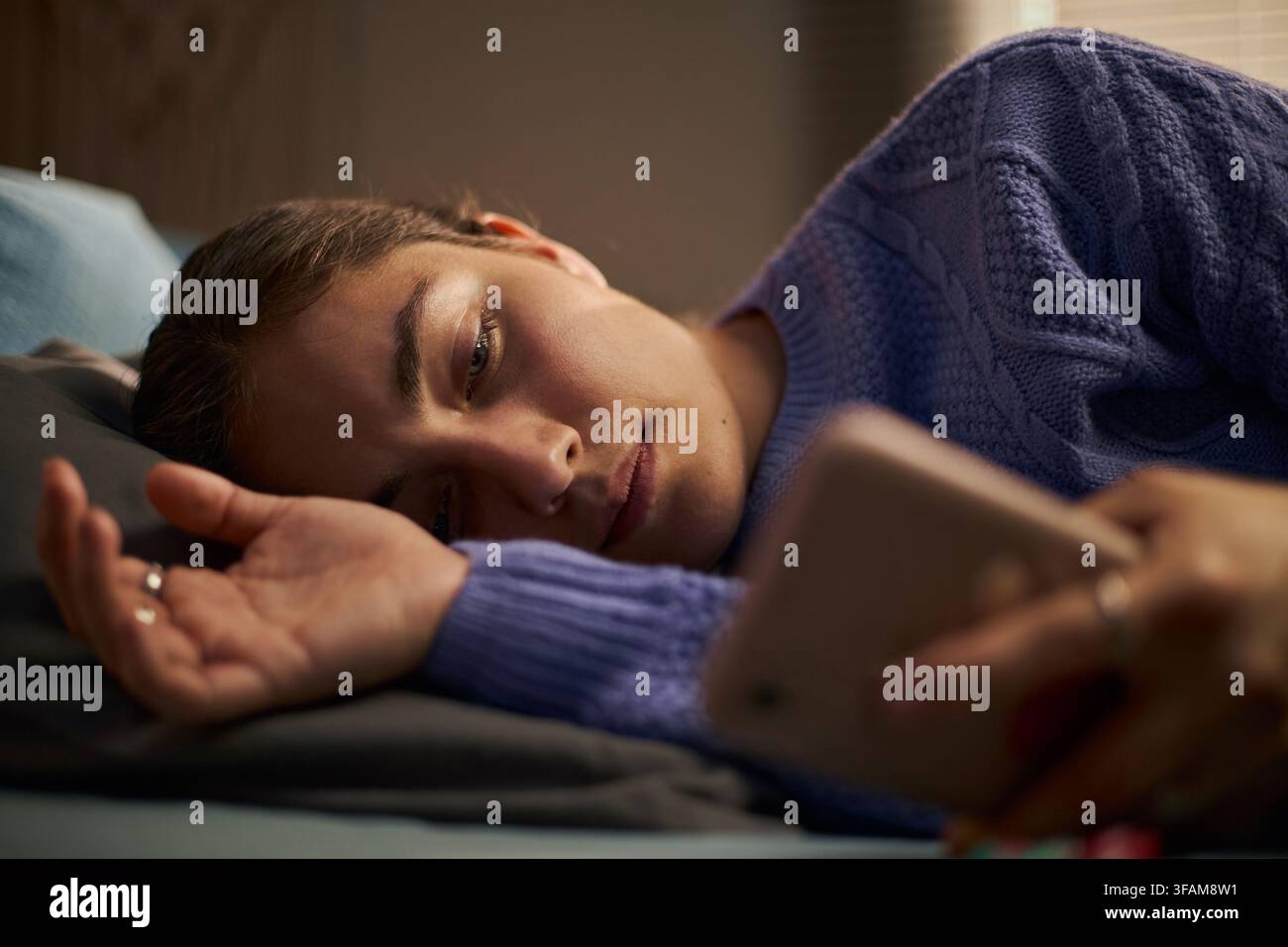 Femme triste allongée dans un lit utilisant un smartphone pour un concept de santé mentale Banque D'Images