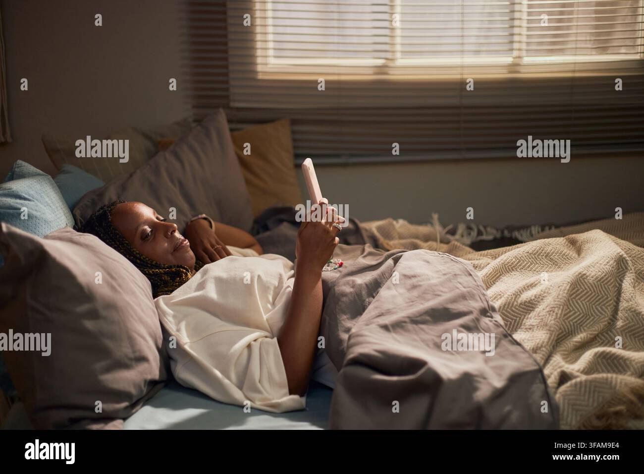 Femme noire allongée dans le lit et utilisant un smartphone le matin Banque D'Images