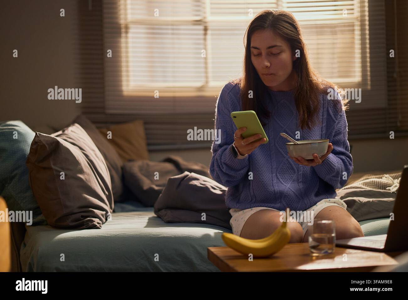 Femme mangeant le petit-déjeuner et utilisant son smartphone au lit Banque D'Images