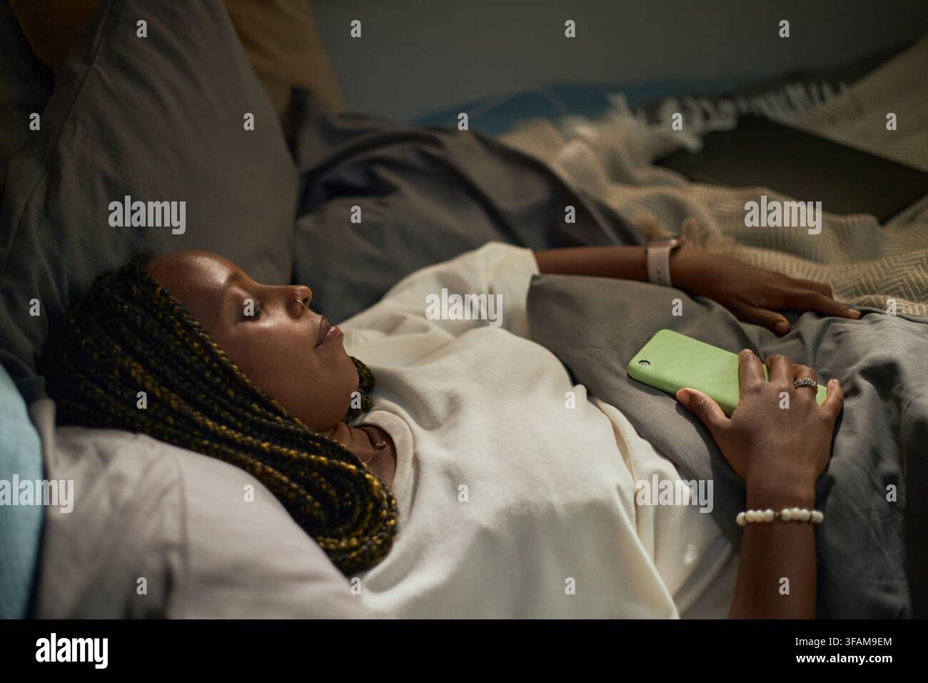 Femme noire dormant au lit tenant un smartphone dans la chambre Banque D'Images