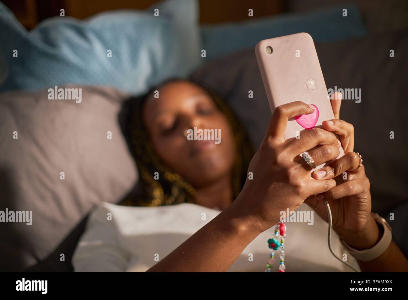 Femme noire tenant un smartphone au lit pour utiliser des applications de médias sociaux Banque D'Images