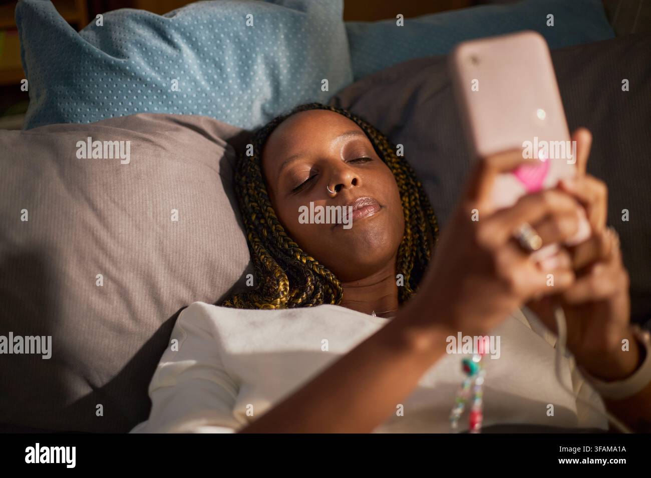 Femme noire allongée dans un lit et utilisant son smartphone pour les réseaux sociaux Banque D'Images