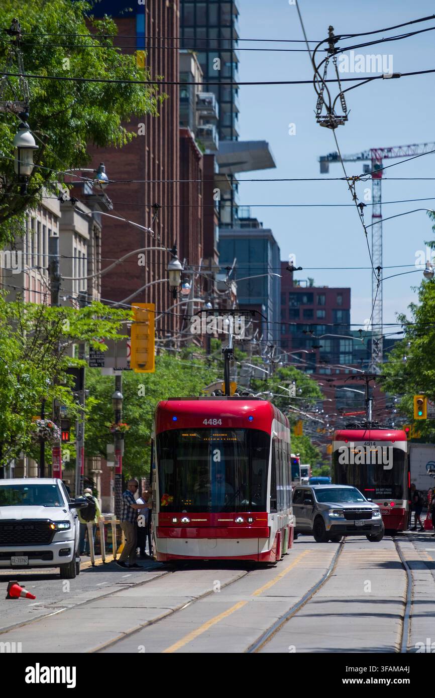Découvrez l'énergie vibrante de Toronto le long d'une rue animée de la ville. Un tramway moderne navigue sur la chaussée, partageant l'espace avec les automobiles et pe Banque D'Images