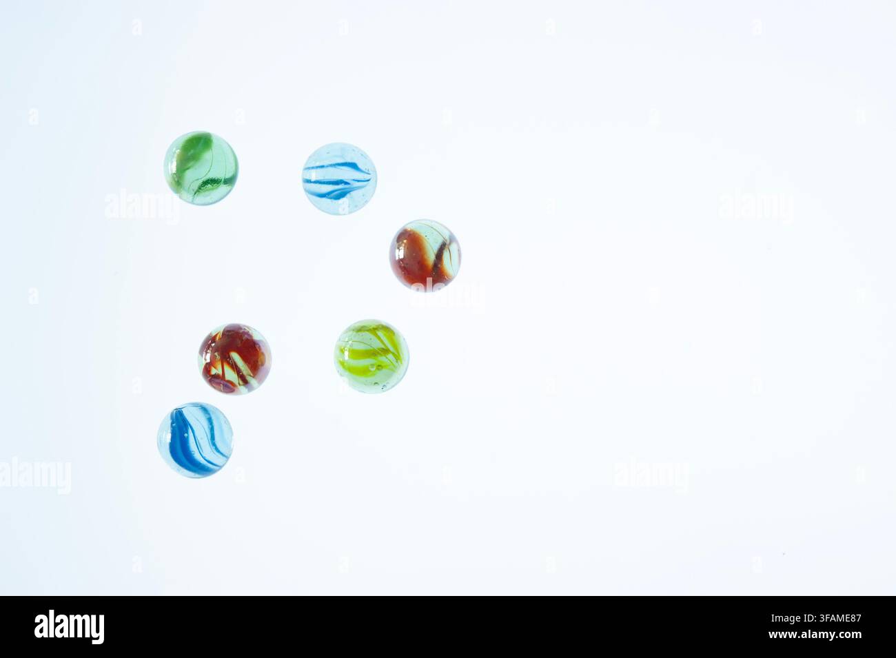 Six billes en verre colorées disposées sur un fond blanc pâle avec un espace de copie généreux, un simple concept de jeu et de collection de l'enfance Banque D'Images