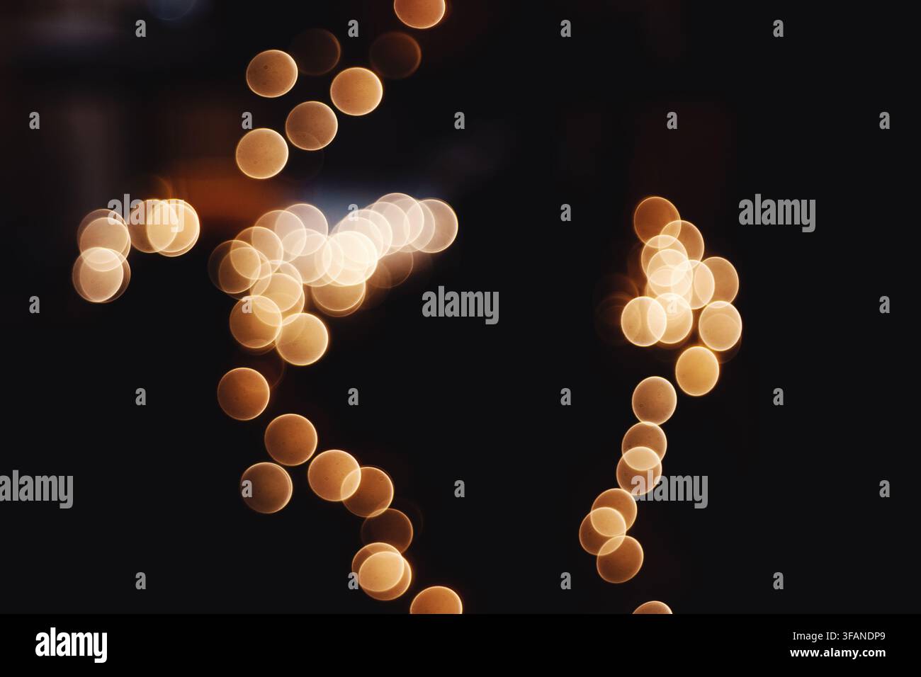 Composition abstraite mettant en scène des lumières dorées bokeh lumineuses créant des motifs circulaires sur un fond sombre. Banque D'Images