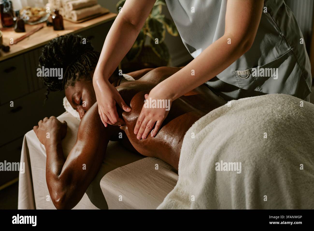 Femme noire recevant un massage du dos d'un thérapeute dans un spa bien-être Banque D'Images