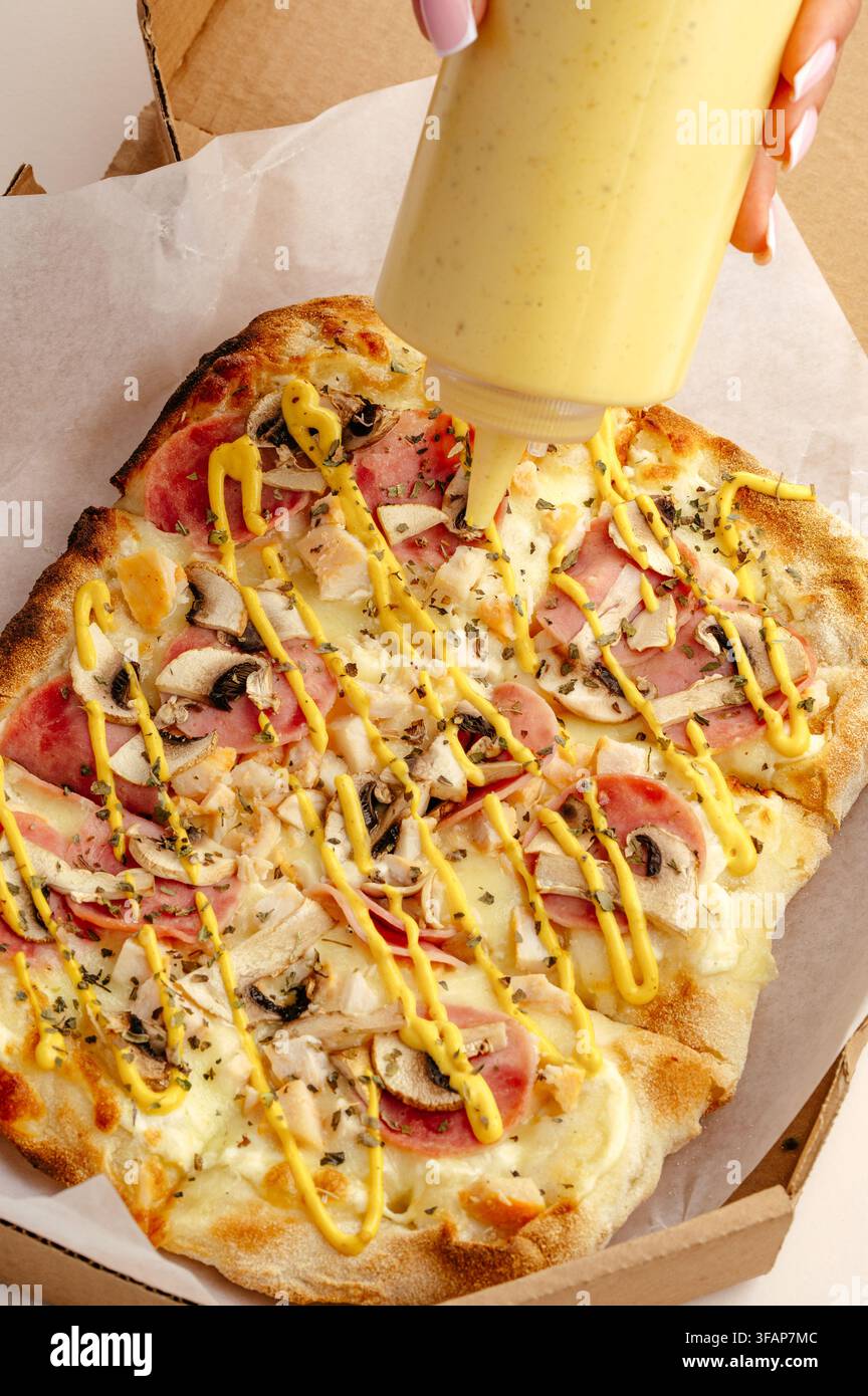 Femme versant une sauce jaune crémeuse sur une pizza Banque D'Images