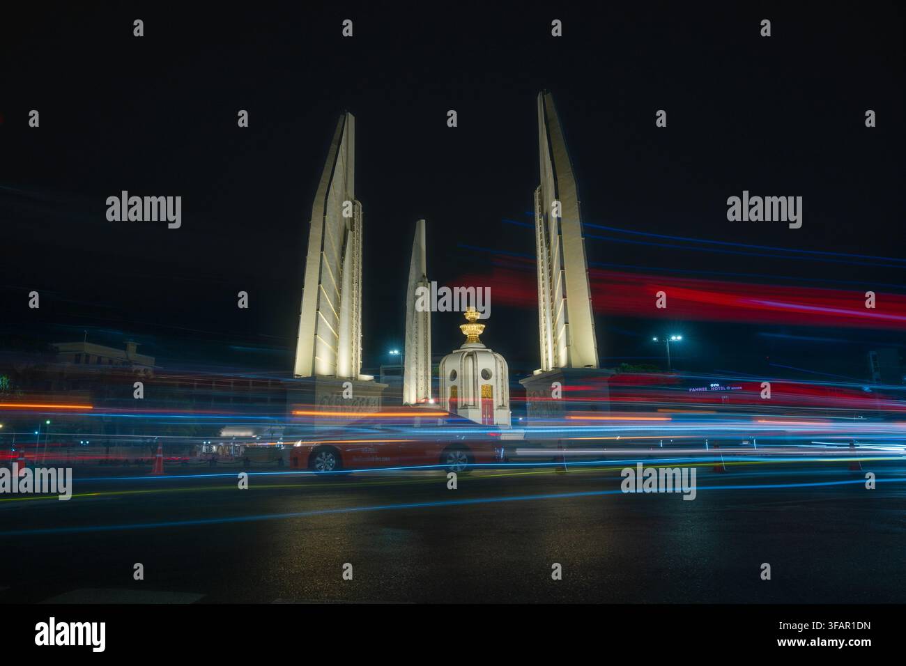 Vue nocturne du Monument de la Démocratie à Bangkok, Thaïlande, avec des lumières colorées de la ville et une flou de mouvement créant une atmosphère urbaine dynamique. Banque D'Images