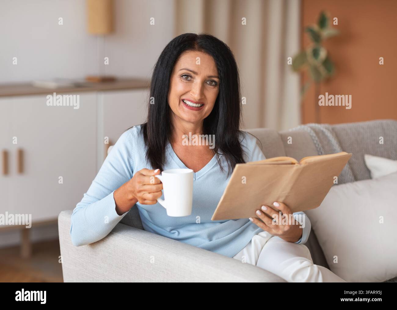 Femme d'âge mûr tenant une tasse de café et un livre Banque D'Images