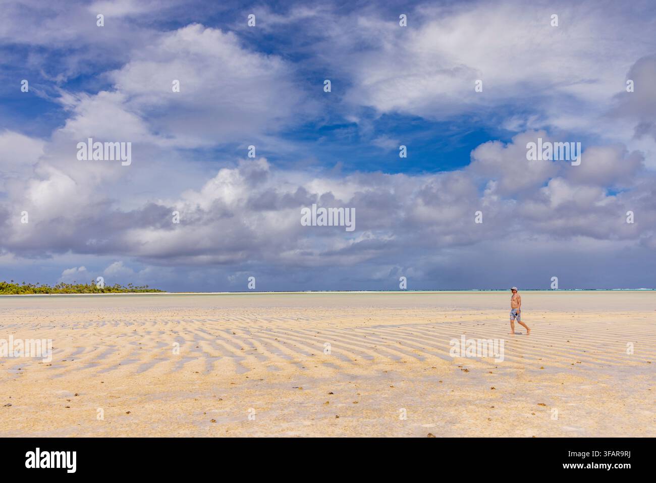 Homme marchant le long de la plage de Honeymoon Island avec un ciel bleu et des nuages sur la lagune d'Aitutaki aux îles Cook Banque D'Images