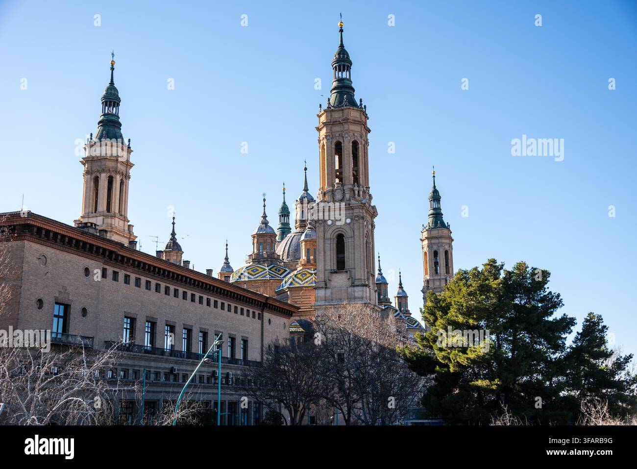 Les hautes tours de la Baslica del Pilar s'élèvent au-dessus des bâtiments et des arbres contre un ciel bleu clair en hiver à Zaragoza, en Espagne Banque D'Images
