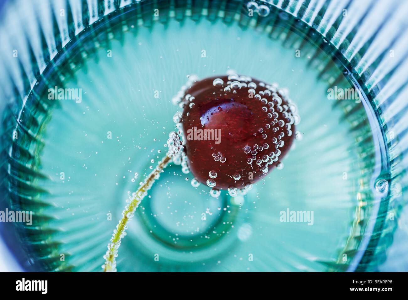 Macro vue de dessus d'une cerise fraîche flottant dans de l'eau pétillante avec de délicates bulles, créant une composition abstraite épurée pour le branding bien-être, boisson Banque D'Images