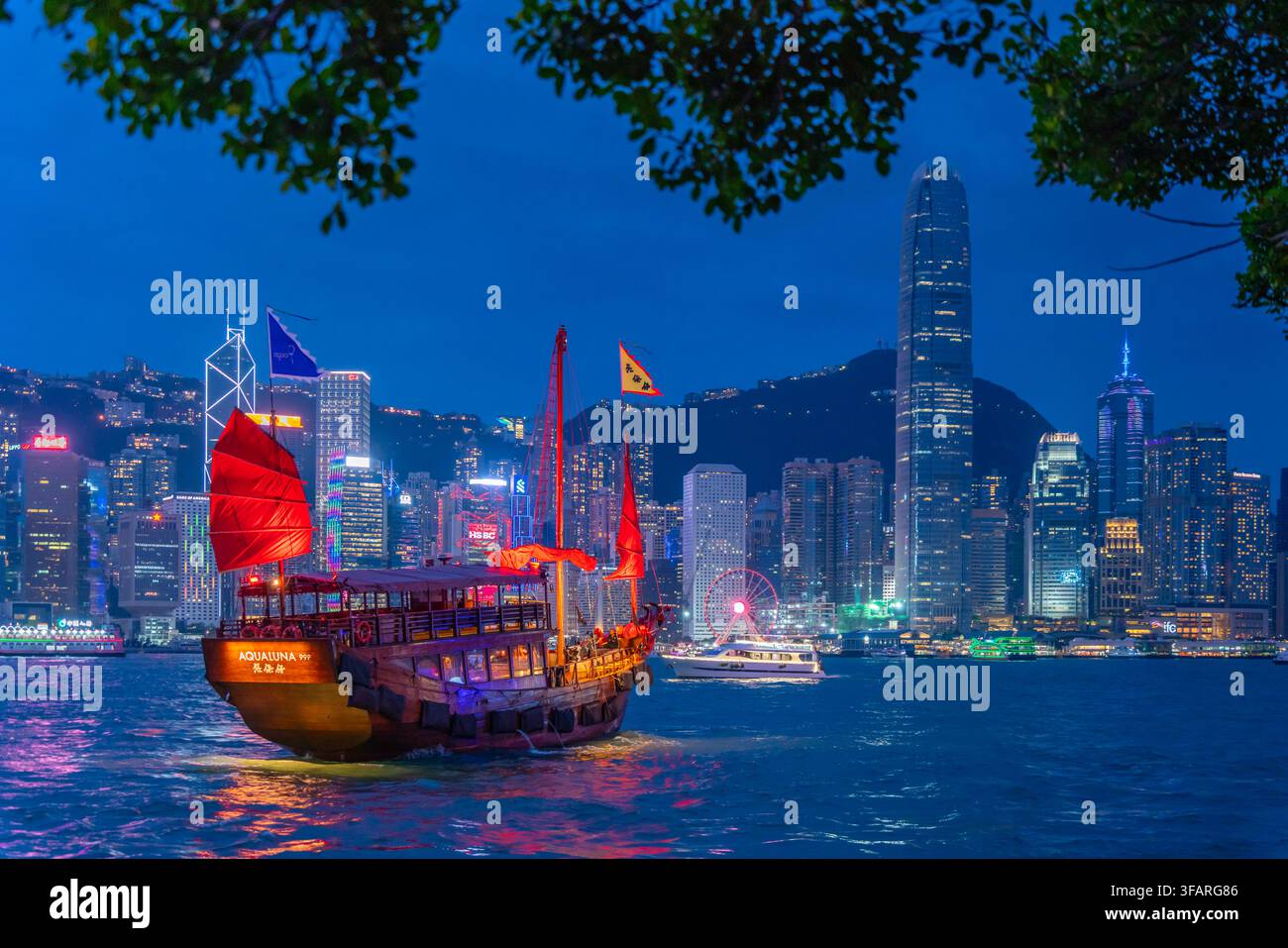 Vue sur la ligne d'horizon de Hong Kong et un bateau-junk à voile rouge depuis Kowloon au crépuscule, Kowloon, Hong Kong, Chine Banque D'Images