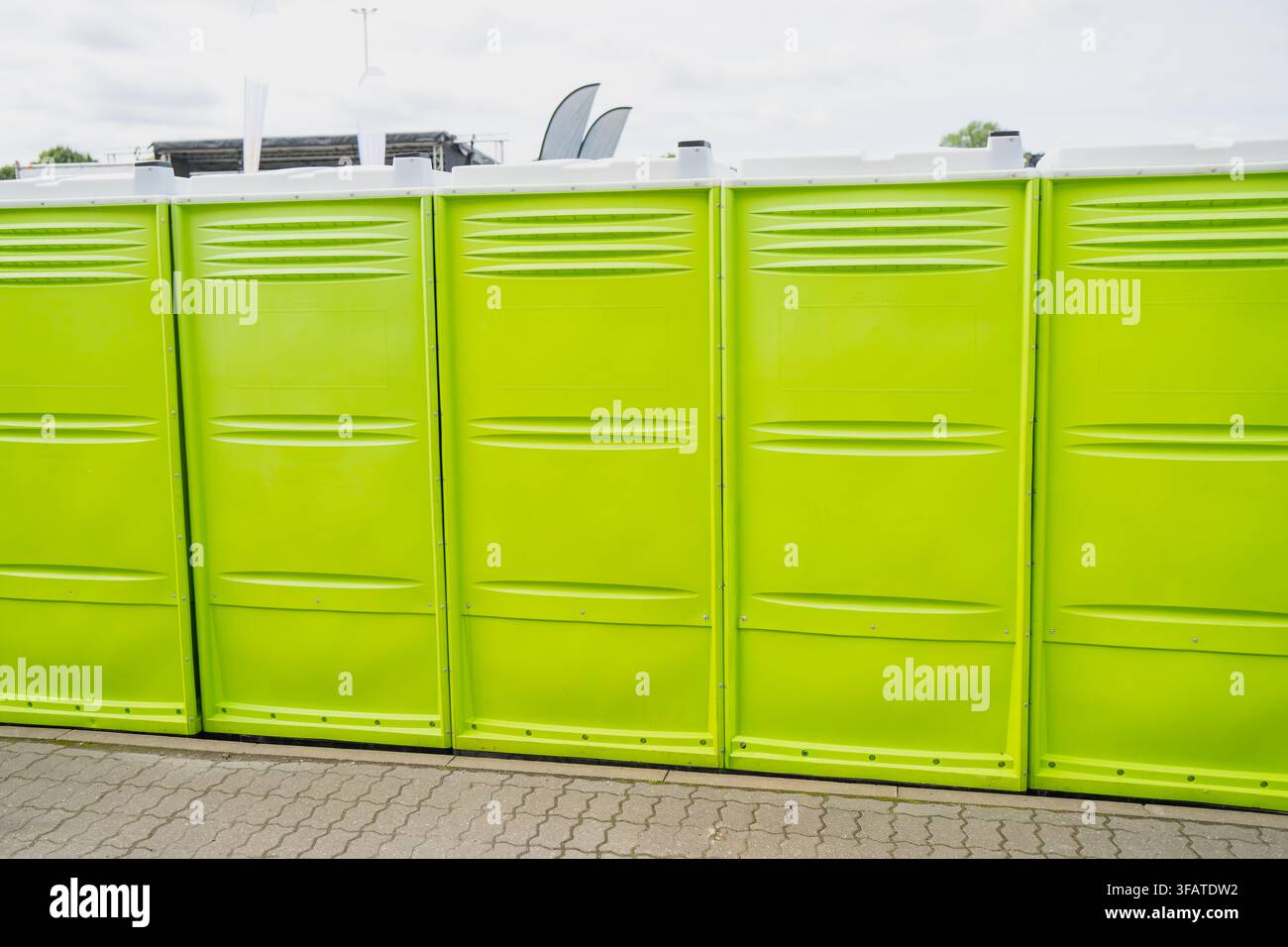 Range de toilettes mobiles vert vif installées sur des briques entrelacées pavées lors de la préparation d’un événement public en plein air ou d’un festival Banque D'Images