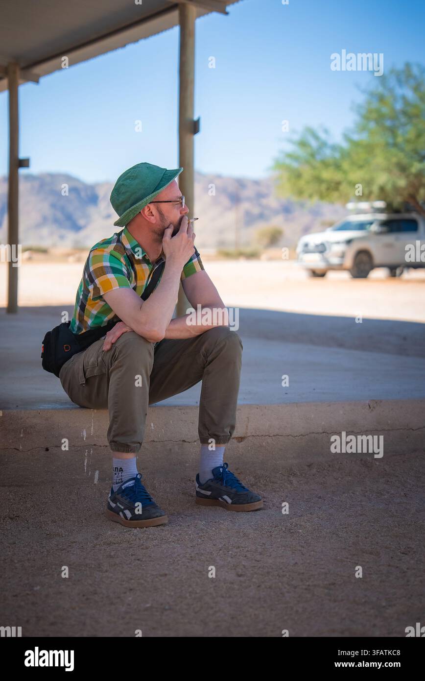 Un homme portant un chapeau se repose et fume en plein air en Namibie Banque D'Images