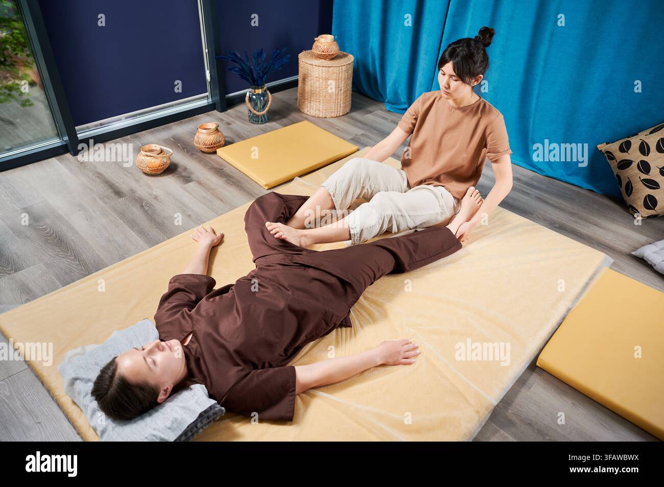 Masseuse faisant massage yoga thaïlandais. Thérapeute de femme faisant le traitement de massage traditionnel pour la patiente féminine à l'intérieur. Client allongé sur tapis, méditant, profitant d'un massage des mains dans une atmosphère calme. Banque D'Images