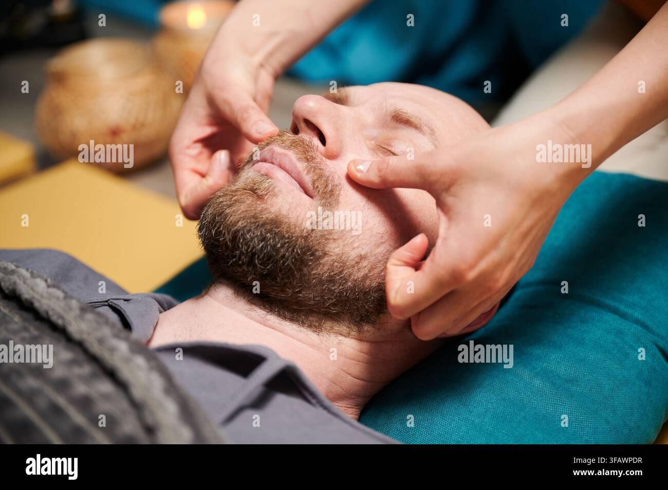 Gros plan d'un homme se faisant masser le visage thaïlandais. Masseuse faisant le traitement de massage traditionnel pour patient masculin. Client chauve avec les yeux fermés, méditant, profitant du massage des mains dans une atmosphère calme. Banque D'Images