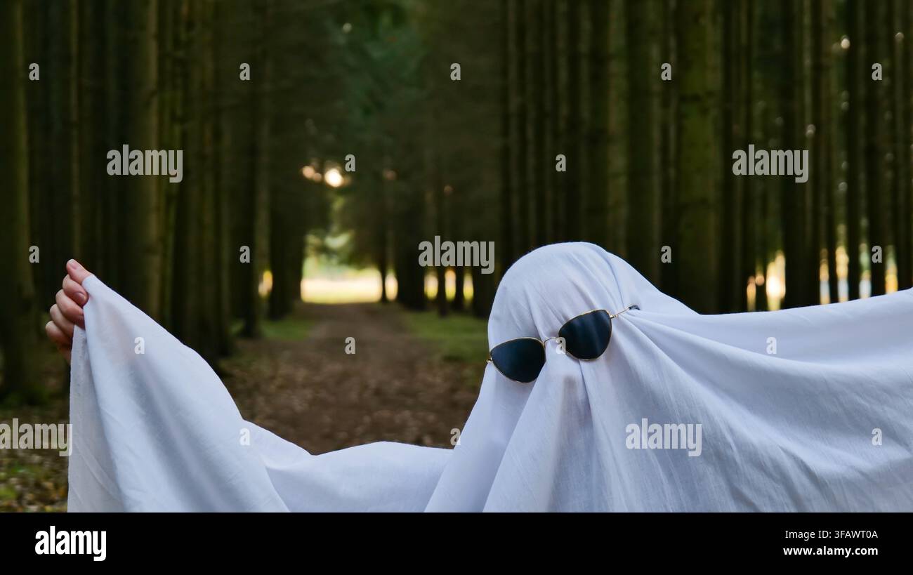 Person en costume de fantôme avec des lunettes de soleil debout sur un sentier forestier Banque D'Images